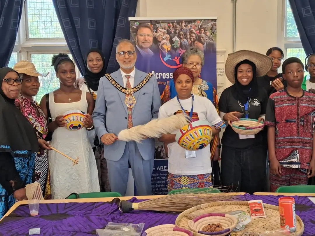 A group of adults and young people standing together indoors holding decorated bowls and woven baskets, with the Lord Mayor of Manchester in ceremonial chains at the centre.